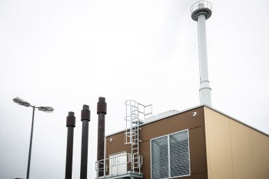 Energiezentrale im H 130. Braunes Gebäude mit mehreren kleinen, braunen und einem großen, weißen Schornstein.