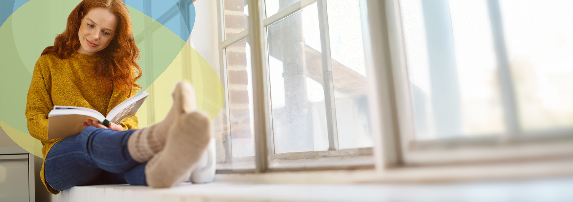 Frau sitzt entspannt auf dem Sims eines Fensters und liest ein Buch an einem kalten Tag, symbolisiert die komfortable Fernwärmeversorgung der SWBB über den Tarif Schönbuch Wärme.