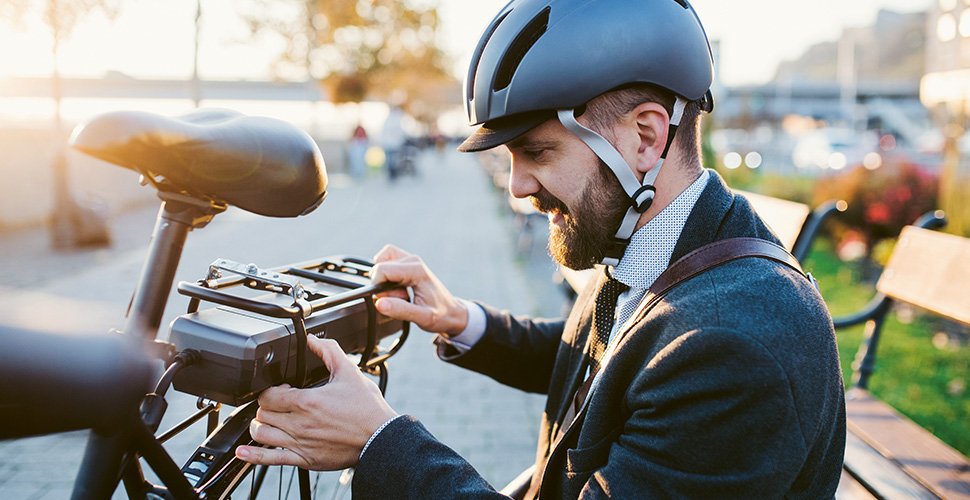 Lächelnder Mann mit Fahrradhelm hantiert mit dem Akku im Gepäckträger seines E-Bikes