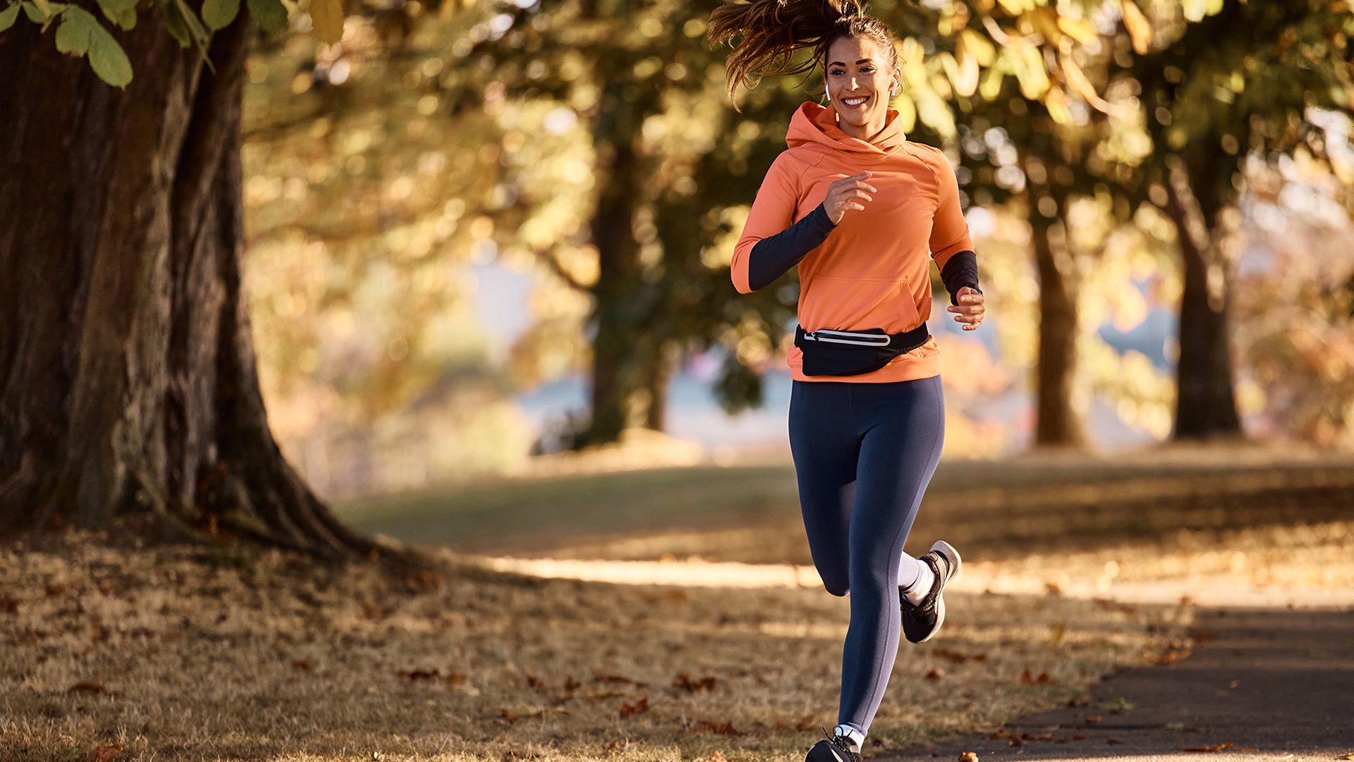 Lächelnde Frau in Sportkleidung joggt in einem herbstlichen Wald.