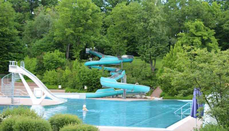 Bild mit beiden Wasserrutschen des Freibad Böblingens. Unten im Becken schwimmt eine Frau. Viele grüne Bäume im Hintergrund.
