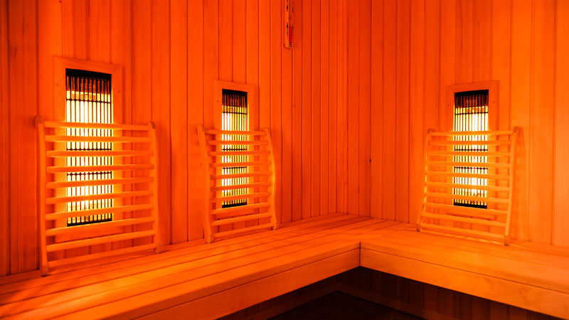 Drei Lampen in den Innenwänden einer Holzsauna, die in rotes Licht getaucht ist