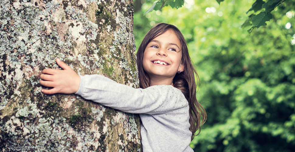 Lächelndes Mädchen umarmt einen Baum